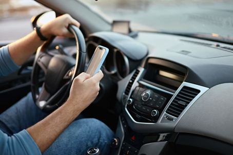 Man using cell phone while hands on steering wheel in car